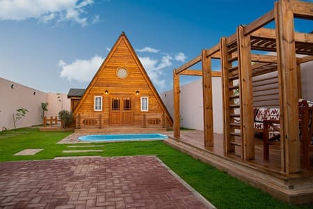 Casa triangolare in legno vista dal giardino, con patio in legno e piscina all'esterno. Usata come attività commerciale airbnb